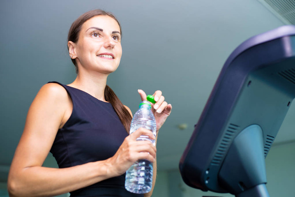 Beautiful fitness girl running and drinking water on treadmill at the gym - Foto, immagini