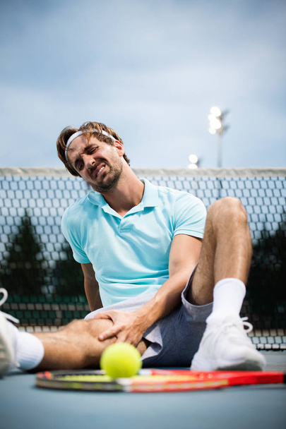 Sports injury. Tennis player touching his knee while sitting on the tennis court - Foto, imagen