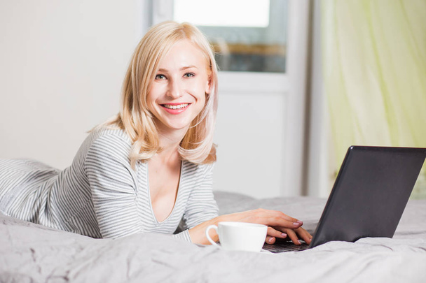 Pretty woman using laptop while having a cup of coffee on bed - Foto, Imagen