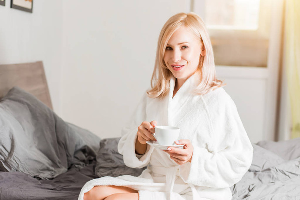 Woman in bathrobe relaxing in her bed in the morning with coffee - Фото, зображення