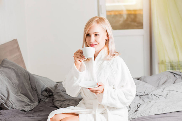 Woman in bathrobe relaxing in her bed in the morning with coffee - Foto, Bild