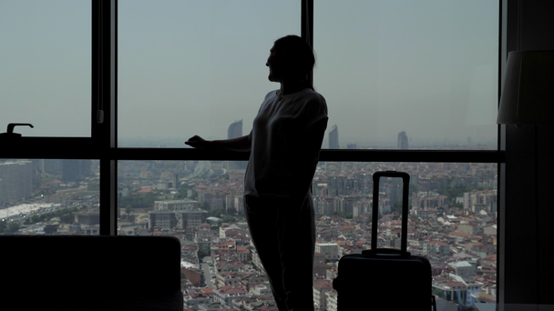 silhouette de jeune fille voyageuse avec valise entre dans la chambre d'hôtel avec vue panoramique sur la ville
. - Séquence, vidéo