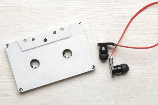 Pequeños auriculares rojo-negros y casete de audio sobre un fondo de madera blanco. vista superior
 - Foto, Imagen