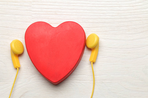 Małe żółte słuchawki i czerwone dekoracyjne serce na białym tle drewnianym. Widok z góry - Zdjęcie, obraz