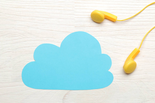 小さな黄色のヘッドフォンと白い木製の背景に紙の青い雲。トップビュー - 写真・画像