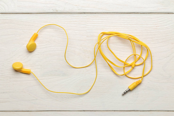 Pienet keltaiset kuulokkeet älypuhelimeen valkoisella puupohjalla. ylhäältä
 - Valokuva, kuva