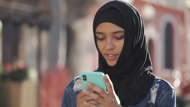 Young beautiful Muslim woman using smartphone standing on the old city background. She having good news on smartphone. - Footage, Video