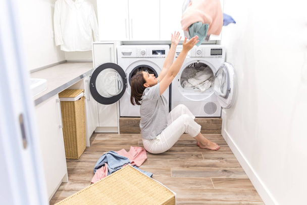 Gelukkige familie moeder huisvrouw in wasruimte met wasmachine gooien kleren omhoog - Foto, afbeelding