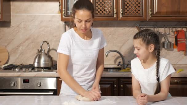 Mom is teaching her teen daughter how to cook dough in the kitchen at home. - Záběry, video
