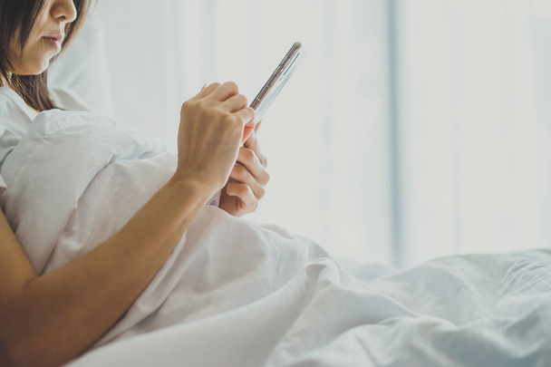 Азиатская девочка в спальне на кровати с мобильным телефоном.
  - Фото, изображение