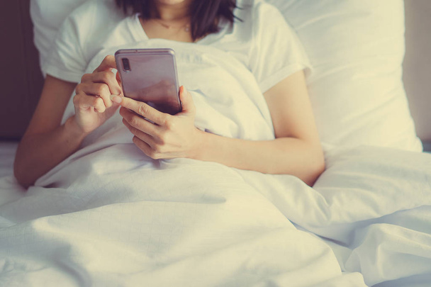 Asian Girl in bed room on the bed with the mobile phone.Closeup  - Photo, image