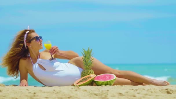 The woman drinks fresh orange juice background the sea. Young beautiful woman lying by the sea on the sand, drinks orange fresh juice. Concept vacation. - Footage, Video