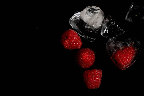raspberries and chunks of ice on a black background. - Foto, Imagen