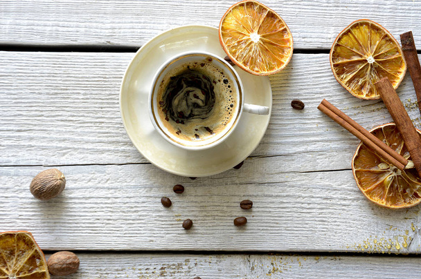 Dried orange slices, fragrant cinnamon sticks and coffee beans with a cup of coffee on a wooden table - Фото, зображення