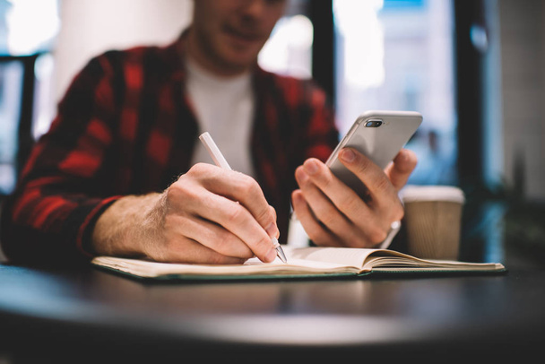 Blurred man with smartphone writing in notebook - Fotografie, Obrázek