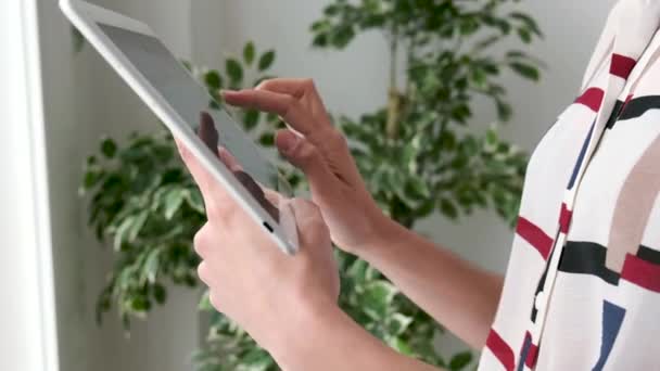 Video of the hands of a woman using the digital tablet while standing in the office. - Video