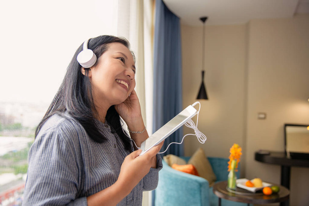 Πανέμορφο χαρούμενο Ασίας γυναίκα ακουστικά ακούγοντας μουσική από το τραπέζι - Φωτογραφία, εικόνα