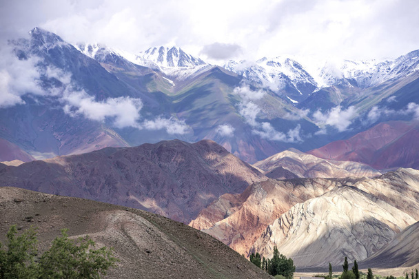 Θέα στα πολύχρωμα βουνά και τις χιονισμένες κορυφές με σύννεφα πάνω τους. Ταξίδι Κιργιζίας - Φωτογραφία, εικόνα