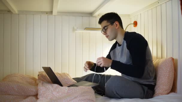 Young man watching video on laptop at the bed in hostel room - Footage, Video