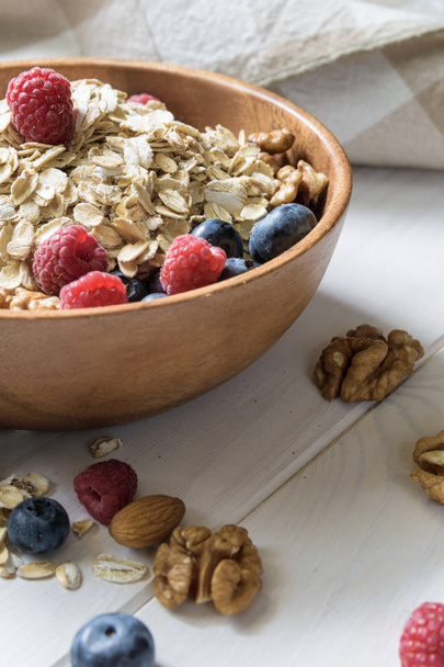 oatmeal with blueberries, raspberries, almond and walnuts in a wooden bowl on a black wooden table - Fotoğraf, Görsel