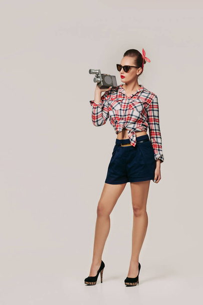pin-up girl in plaid shirt holding old vintage camera. - Foto, afbeelding