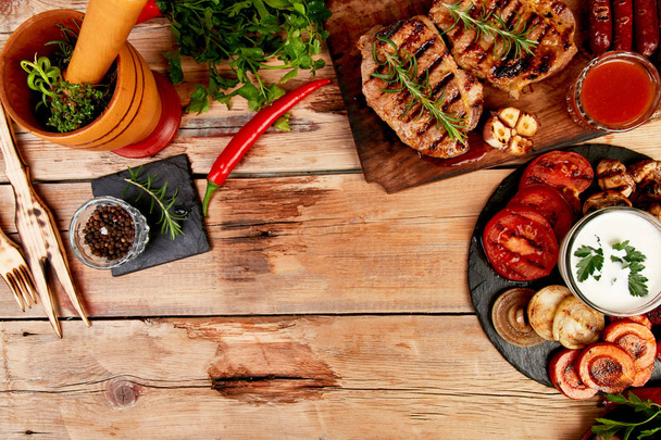 Grilled meat. Steak pork grill on wooden cutting board with a variety of grilled vegetables on  rustic background  Top view. Flat lay. Copy space. - Photo, Image
