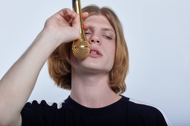 Young handsome caucasian man singing into golden microphone. Concept of party or karaore vocal. Studio, light  background, copy space. - Valokuva, kuva