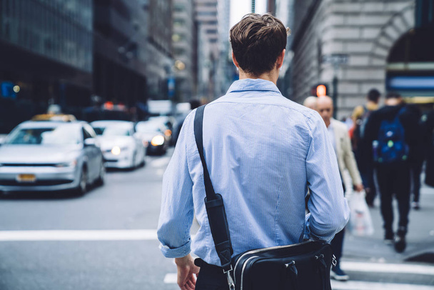 Back view of intelligent male economist with trendy leather briefcase walking to business meeting in financial district, clever professional proud ceo in blue t shirt going to destination in downtown - Fotografie, Obrázek
