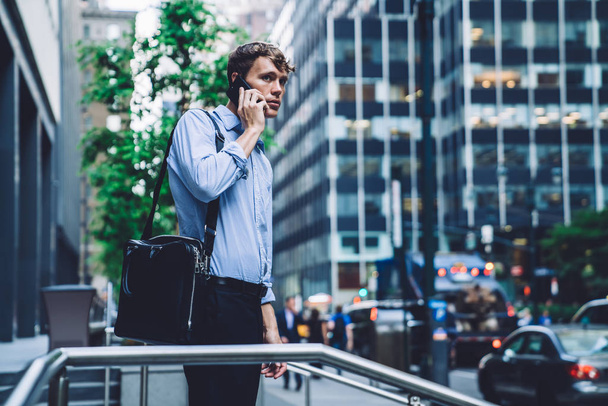 Intelligent businessman with briefcase making online smartphone call for discussing roaming connection with operator, male employee phoning to partner talking during phone conversation outdoors - 写真・画像