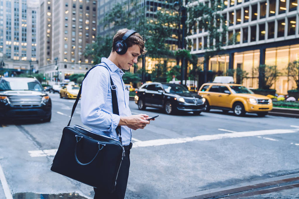 Side view of intelligent man checking received voice message via modern cellphone device listening via noise cancellation headphones, Caucasian male employee with briefcase search text on website - Photo, Image