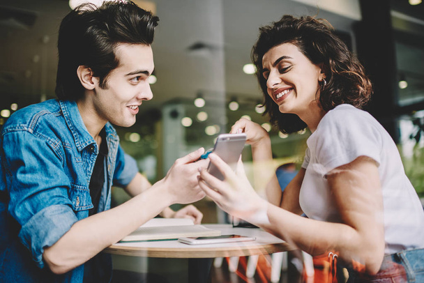 Happy smiling man and woman watching funny video online on content website via cellular phone, positive caucasian friends enjoying communication via smartphone gadget during free time in cafeteria - Photo, image