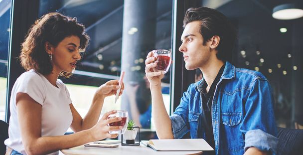 Stylish couple in love sitting coffee table in cafe and drinking juice during meeting.Young man and woman dressed in casual wear spending free time together in modern cafeteria interior - Photo, Image