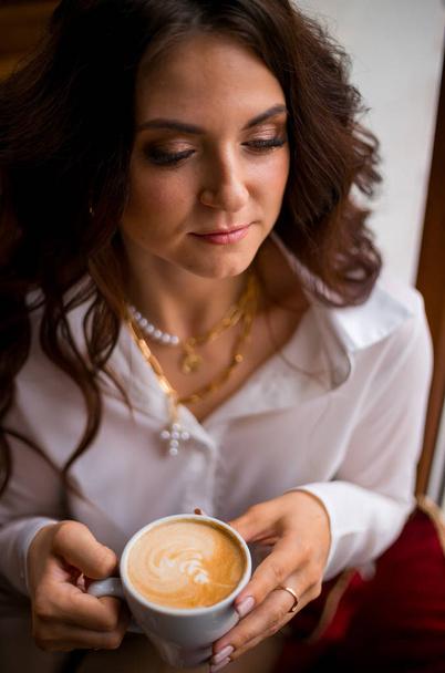 Beautiful stylish brunette woman drinking coffee in a cafe and smiling with her eyes closed. - Photo, Image