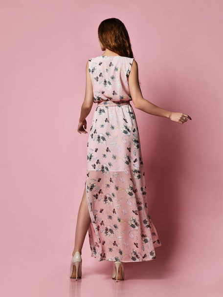 Woman back in a silk pale pink dress looking at the camera in full growth. Cute girl in romantic clothes is going on a date, smiling pretty on a pink background - 写真・画像