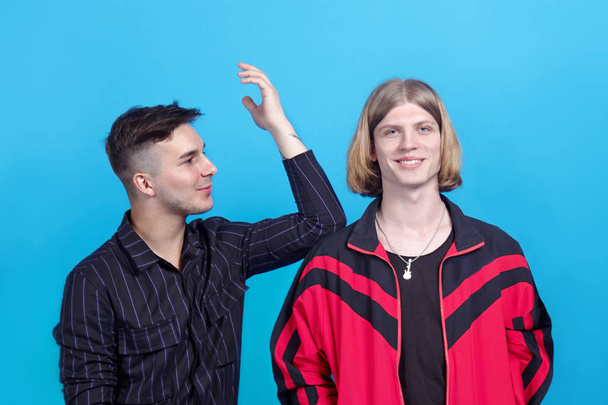 Two young handsome guys, talk to each other, smiling. Gay relationship or close friendship. Indoors, studio portrait, copy space, blue background. - Photo, image