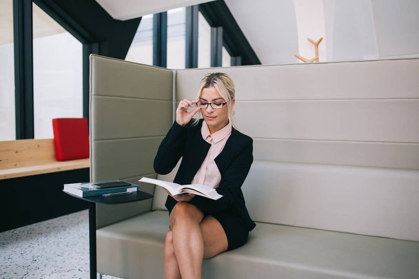 Concentrated female executive manager reading literature book with technology information, confident caucasian woman in stylish spectacles for vision correction interested on financial book - Photo, image