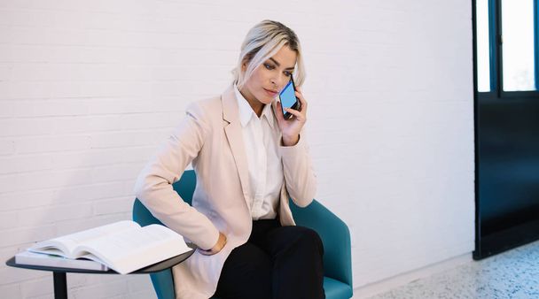 Serious businesswoman calling to employee for discussing business contract connected to 4g wireless, blonde female lawyer sitting near table with textbook and using wifi for making conversation - Foto, immagini