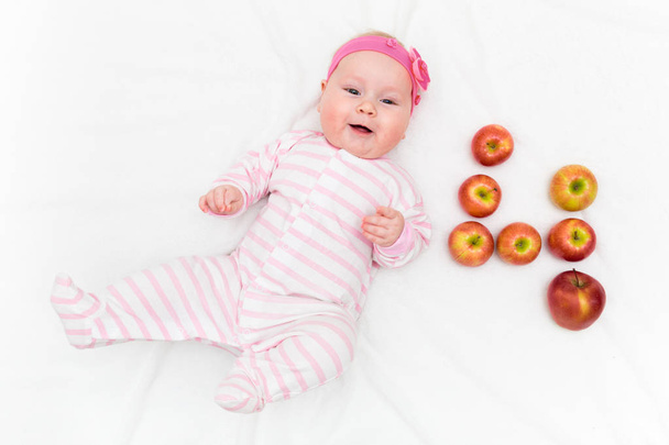 Linda niñita acostada sobre fondo blanco con manzanas rojas y verdes frescas en forma de número cuatro
 - Foto, imagen