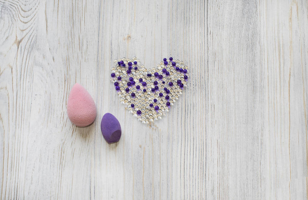 Růžové a fialově krásné Blendery, houbičky na dřevěné šedé pozadí. Kosmetické nástroje pro makeup a hydrogelové kuličky ve formě srdce. - Fotografie, Obrázek