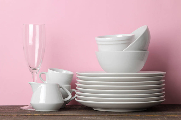 Cölöpök fehér kerámia edények, tányérok, csészealjak, csészék rózsaszín háttér. Konyhai. - Fotó, kép