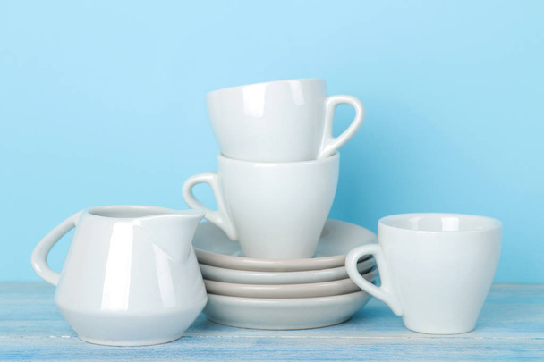 Pilhas de utensílios de mesa de cerâmica branca, pires e copos em um fundo azul suave. utensílios de cozinha
. - Foto, Imagem