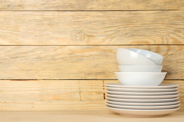 Кучи белой керамической посуды, тарелки, тарелки и чашки на естественном деревянном фоне. кухонные принадлежности
. - Фото, изображение