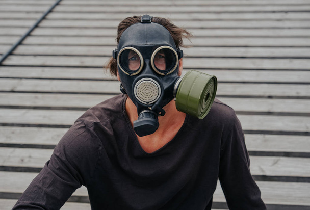 Man in a dirty city in gas mask looks into the town skyline - 写真・画像