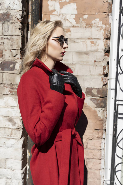 A beautiful blond girl wearing a red coat, sunglasses and gloves - Foto, afbeelding