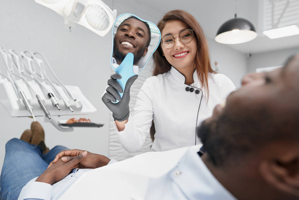 Dentist keeping mirror and showing white smile to patient - Fotoğraf, Görsel