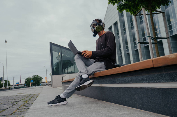 A man in a gas mask in the city with a laptop phone and headphones - Foto, imagen