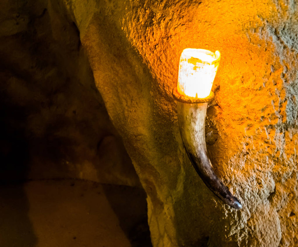 lighted lamp hanging on a cave wall, lighting made out of a animal tusk, underground grotto background - Photo, Image
