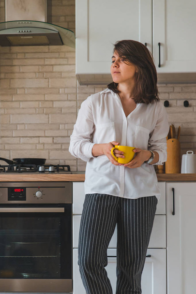 young pretty stylish woman holding yellow mug at white kitchen - Photo, image
