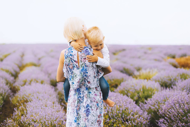 Young blonde woman holding his little son in a lavender field. Pure mother love image. - Photo, Image