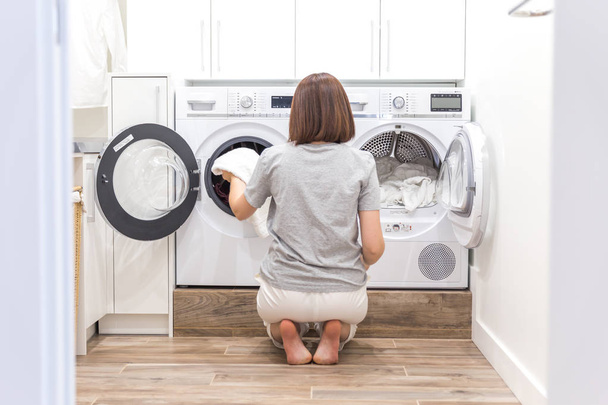 Woman putting clothes to washing machine for wash - 写真・画像